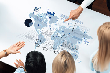 Professionals collaborate over a table displaying digital graphs and charts, analyzing global data and insights to inform business strategies and decision-making. Trope