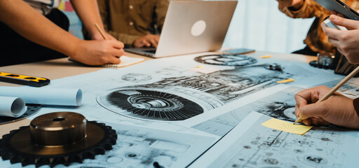 A vibrant scene capturing a collaborative engineering session where team members engage with technical drawings and sketches spread across a modern workspace table. SACTR