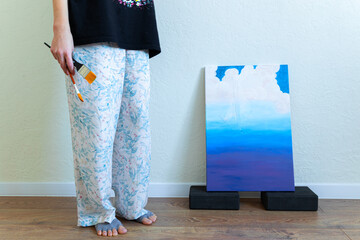 painter woman in home pants and nice socks with brushes in her hand near unfinished picture domestic scene candid people concept comfort zone