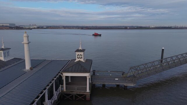 Gravesend Pier with a commuter boat sailing on river Thames. Aerial circular motion above the historic pier. Passenger boat in orange color sailing towards the passenger terminal.
