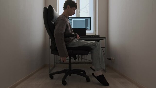 Man adjusting office chair height in modern home office workspace with computer desk, ergonomic furniture setup for comfortable remote work and productivity indoors