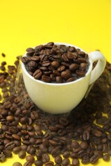Fototapeta premium Aromatic coffee beans and cup on yellow background, closeup