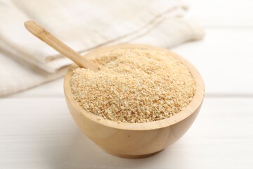Granulated dried garlic in bowl on white wooden table, closeup