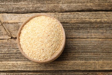Granulated dried garlic in bowl on wooden table, top view. Space for text