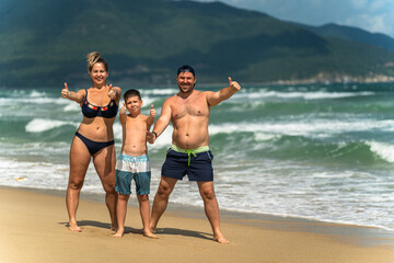 Happy family giving thumbs up while on vacation at the seaside