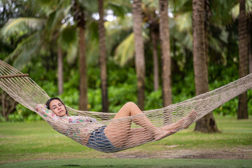 A girl lies in a hammock against a background of green palm tree