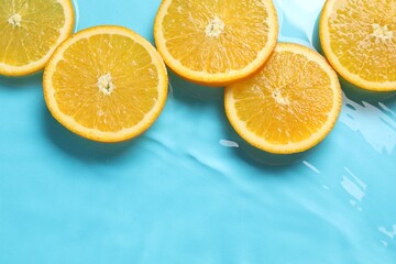 Fototapeta premium Orange slices in water on light blue background, flat lay. Space for text