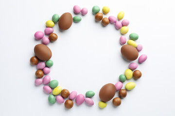Obraz premium Chocolate Easter eggs and candies on white background, flat lay. Space for text