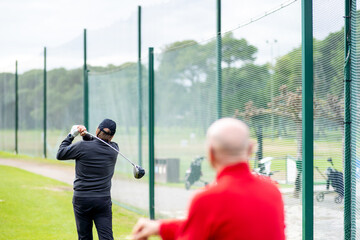 A man is swinging a golf club while another man watches