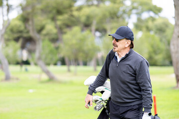 A man in a hat and sunglasses is walking on a golf course with a golf bag