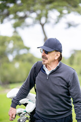 A man in a black hat and sunglasses is walking with a golf bag