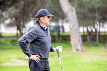 A man in a gray sweater and hat is standing on a golf course
