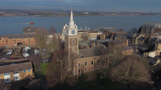 Gravesend town with church and river Thames on a sunny winter day. Aerial view of historic church with bell tower and clock. Circular and forward motion. Passenger ferry crossing river Thames. 