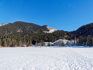 Spitzingsee in Bavarian Alps. Hotel and chalets on the shores of the frozen lake, at the foot of the wooded Schwarzkopf hills, the meadows of the Obere Maxlraineralm and the Taubenstein massif
