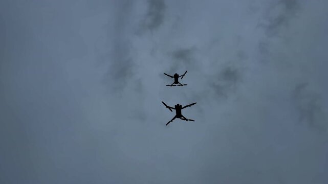Drones fly above the clouds during an event in the afternoon sky. Two drones are flying in the cloudy sky during the afternoon at a local event.