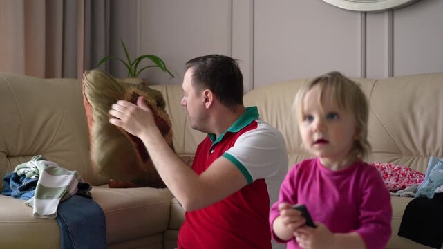 Father and his young daughter share playful moments with stuffed elephant and remote control in their cozy living room.