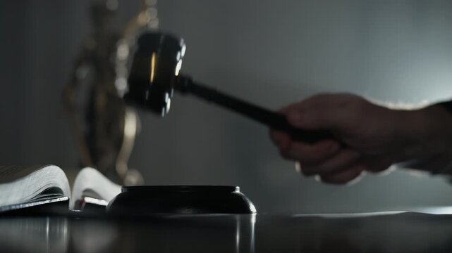 Close-up of a judge striking a wooden gavel on a desk with the Statue of Justice in the background. courtroom authority, legal decisions, rule of law in a dramatic setting.
