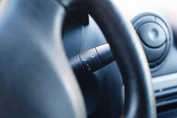 Car windshield wiper control lever closeup. Vehicle interior detail with steering wheel. Automotive dashboard element. Modern car cabin design. Driving control concept. Transportation technology.