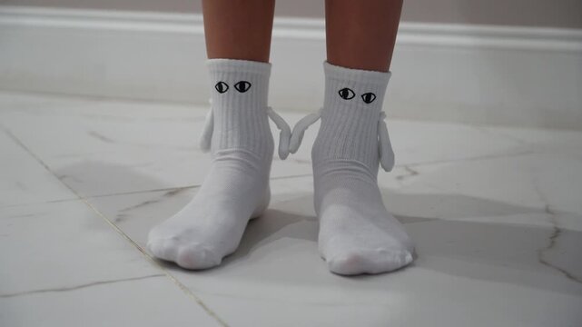 Childs feet clad in playful white crew socks adorned with cartoonish eyes and floppy side ears, standing on polished marble floor.