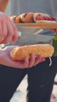 Vertical close-up tilt-up shot of unrecognizable man grilling sosages and making hot dogs at summer lake party