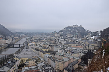 Fototapeta premium Panoramic view of Salzburg on a foggy winter day, with the Hohensalzburg Fortress visible in the background. Atmospheric winter cityscape with historic architecture.