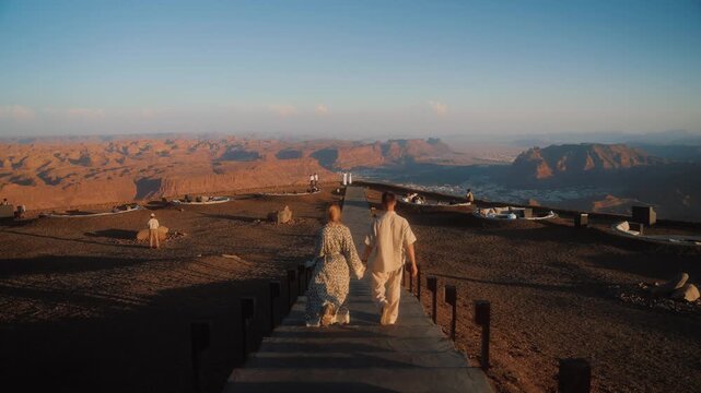 Couple is traveling in Saudi Arabia, AlUla. Man and woman walk away with the view of canyon and sand rocks of Al Ula.