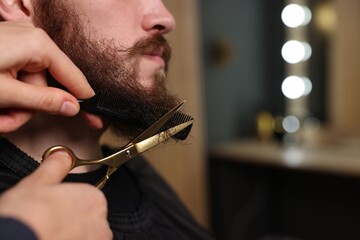 Barber trimming man's beard in barbershop, closeup. Space for text