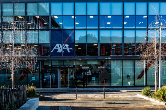 The modern glass facade of Wolfe Tone House in Dublin, featuring the prominent AXA logo, reflected city life on a crisp, bright day.