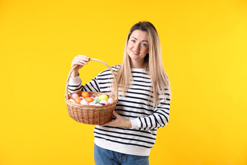 Obraz premium Easter celebration. Smiling woman with wicker basket full of painted eggs on yellow background