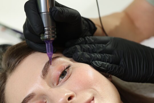 Beautician making permanent eyebrow makeup to young woman, closeup