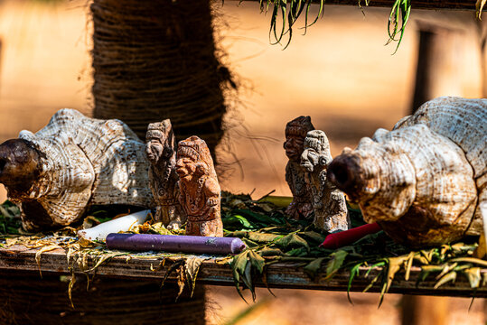 Figuras artesanales de barro con caracoles y velas en entorno natural. Figuras artesanales de barro, caracoles marinos y velas de colores sobre una superficie r&uacute;stica al aire libre. 