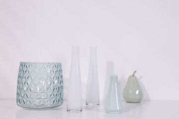 Many stylish vases on white table near light wall, closeup