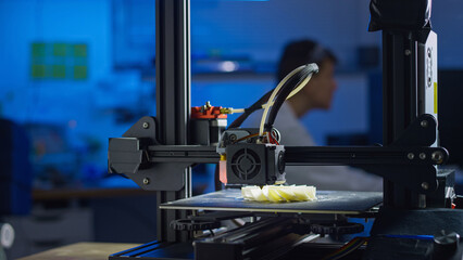 A professional engineer adjusts a 3D printer in a lab while monitoring the printing process for precision.