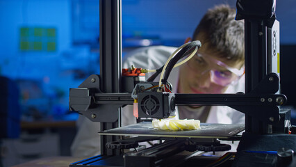 Professional engineer in lab coat and safety glasses adjusts 3D printer while overseeing product development and precision fabrication.