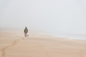 man and his dog walking on a foggy morning at the beach