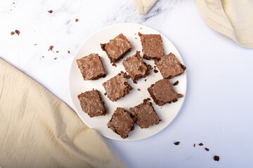 Top view of a chocolate brownie cut into pieces on a white plate.