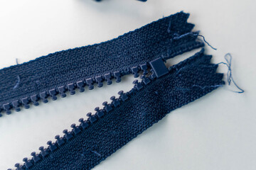 Close-up view of a broken navy zipper with frayed fabric edges on a light background, highlighting the details of the zipper teeth and pull tab for textile repair projects © Андрей Знаменский