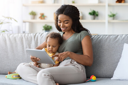 Babies And Gadgets. Happy Black Woman And Her Toddler Son Using Digital Tablet While Relaxing Together On Couch In Living Room, Mom And Child Shopping Online Or Browsing Internet, Closeup