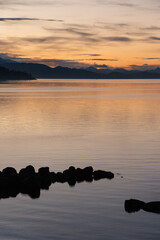 orange sunset on the shores of the lake with mountains in the background
