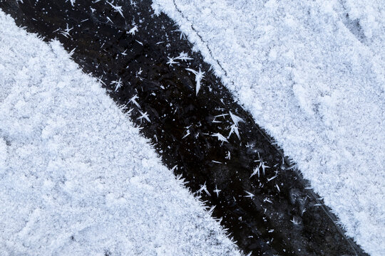 Close-up of snow and snowflakes on a frozen lake in Finland in winter, viewed from above. Diagonal stripe of black ice. Abstract full frame textured wintry background. Copy space, top view.