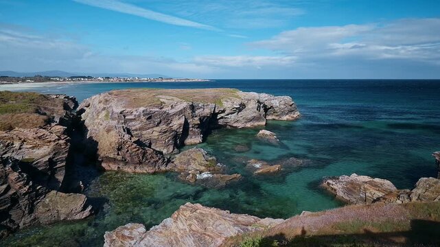 Beautiful panoramic landscape of the famous Las Catedrales beach, also known as beach of the Cathedrals, featuring impressive rock formations, clear turquoise water, and a picturesque coastline