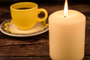 Fototapeta premium Lit Candle with Blurred Coffee Cup in Background