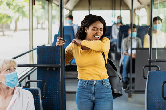 Black lady sneezing and coughing in elbow standing inside public transport without mask, holding handle ignores warning and health advice about covid, risks spreading infectious disease, people scared