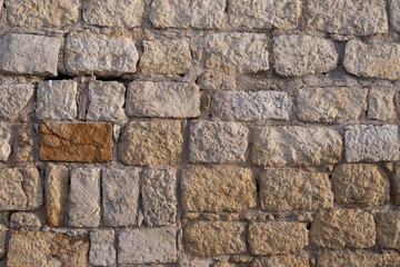 Fototapeta premium Detailed texture of a weathered stone wall made of rough limestone blocks. The surface shows natural erosion, cracks, and warm tones, ideal for architectural, historical, or design backgrounds.