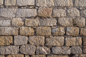 Obraz premium Detailed texture of a weathered stone wall made of rough limestone blocks. The surface shows natural erosion, cracks, and warm tones, ideal for architectural, historical, or design backgrounds.