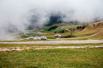 Seceda mountain landscape with scattered chalets and fog rolling in the Dolomites