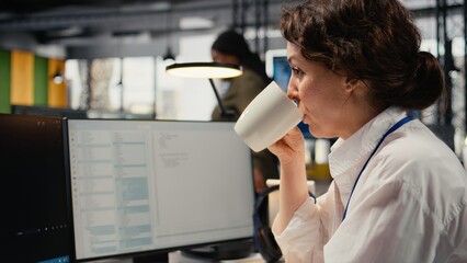Close up of developer enjoying coffee while working in AI startup training predictive models for language processing tasks. Tech expert drinks beverage, uses technical expertise for IT tasks, camera A