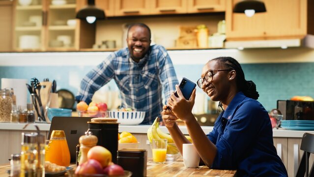 Black girlfriend taking photos of her and boyfriend on the smartphone, laughing and enjoying time together. Happy couple feeling happy in their relationship, joyous woman at home.
