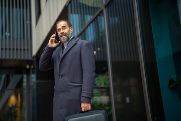 Fototapeta premium Senior businessman talking on phone outside modern office