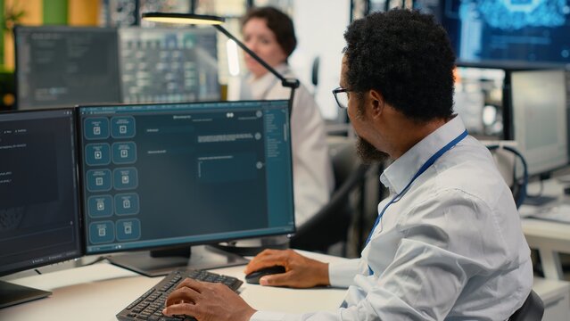 Programmer in office using AI LLM chatbot to get help optimizing systems performance metrics. IT worker in tech agency utilizing generative AI LLM assistant for faster software development, camera B